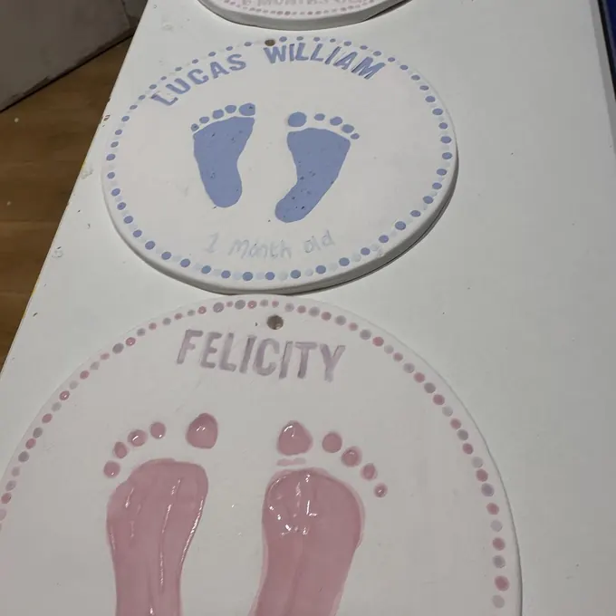 Two glazed keepsake plates with pink baby footprints and names
