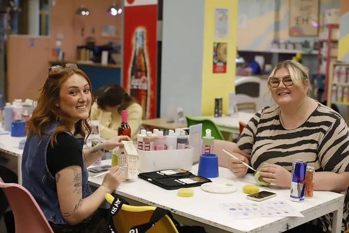 Two friends laughing while painting pottery at a studio table